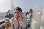 Businesswoman using cell phone on sunny urban pedestrian bridge, London, UK