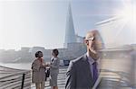 Businesswomen with digital tablet talking on sunny urban bridge, London, UK