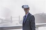 Businessman using virtual reality simulator glasses on sunny urban bridge over Thames River, London, UK