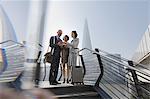 Business people with suitcase using digital tablet on sunny waterfront, London, UK