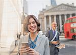 Portrait smiling businesswoman texting with cell phone on urban city street, London, UK