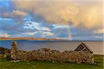 Remains of a stone house on the Isle of Skye with a rainbow appearing over the coast in Scotland, United Kingdom