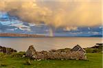 Remains of a stone house on the Isle of Skye with a rainbow appearing over the coast in Scotland, United Kingdom