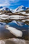 Riffelsee Lake with melting snow and reflections of the snow covered mountains of the Swiss Alps in spring at Zermatt, Switzerland