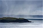 Sunlit sea cliffs and rainclouds along the coast of the Isle of Skye in Scotland, United Kingdom