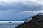 Sunlit ocean with sea cliffs and rain clouds along the coast of the Isle of Skye in Scotland, United Kingdom