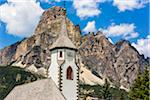 Close-up of the steeple of the St Caterina Parish in the township of Corvara with mountain tops of the Dolomites in the background in South Tyrol, Italy