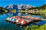 Paddle boats for rent at a dock with the Grand Hotel Misurina in the background reflected in Lake Misurina on a sunny day in the Dolomites in Veneto, Italy