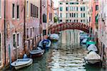 Motorboats moored along a canal with a footbridge in the background in Venice, Italy