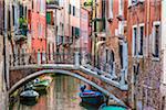 Stone footbridge with iron railing crossing a canal lined with historical buildings in Venice, Italy