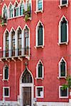 Close-up facade of a tradtional stone building in red stucco with ornate window frames in Venice, Italy