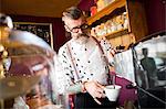 Quirky vintage senior man preparing coffee behind cafe counter