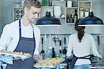 Chef in kitchen, holding baking trays of canapes