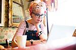 Quirky woman using laptop in bar and restaurant, Bournemouth, England