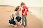 Young woman rolling up son's jeans on beach