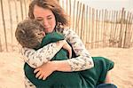 Young woman on beach hugging son wrapped in blanket