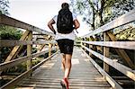 Rear view of young male runner running across rural footbridge