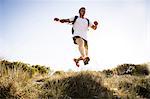 Young man training, jumping mid air from sand dunes