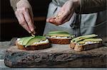 Woman sprinkling chopped walnuts onto avocado bruschetta, mid section