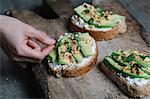 Woman placing herbs on ricotta, avocado and walnut bruschetta, close-up