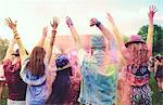 Rear view of young adult friends dancing and throwing coloured chalk powder at festival