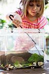 Girl scooping fishing net in plastic tadpole pond on garden table