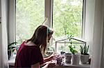 Young woman tending potted plants on windowsill