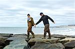Young sea fishing couple stepping over beach rocks