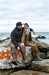 Young sea fishing couple sitting on beach rocks