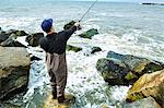 Young man standing on rock sea fishing