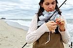 Young woman in waders preparing fishing rod line on beach