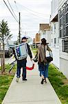 Rear view of young couple carrying fishing equipment on sidewalk
