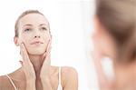 Young woman looking in mirror, applying moisturiser to face