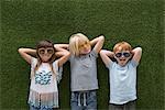 Children in front of artificial turf wall, hand behind head wearing sunglasses
