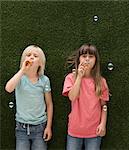 Children in front of artificial grass wall blowing bubbles