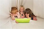 Children lying in bed looking at digital tablet