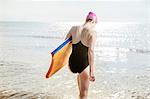 Young woman carrying surfboard in sea, Folkestone, UK