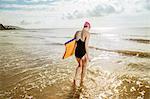 Young woman carrying surfboard in sea, Folkestone, UK