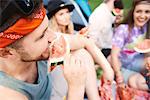 Young boho adult friends eating melon slices at festival