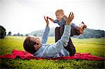 Mid adult man lying on back balancing baby son in rural field