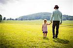 Rear view of girl strolling with father in rural field