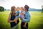 Mid adult couple kissing daughter and baby son on cheek in rural field