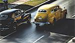 High angle shot of two classic 1950s cars driving on a road.