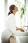 A woman standing at a sink in a bathroom and looking at herself in a mirror.