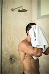 A man standing in a bathroom, drying himself with a towel.