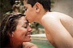 A boy kissing the forehead of a woman in a swimming pool.