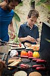 A man and boy standing at a barbecue cooking food.