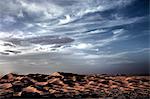 Desert landscape with sand dunes under a cloudy sky.