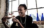 Smiling young woman sitting indoors by a window, eating slice of pizza.