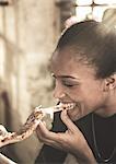 Close up of young woman eating slice of pizza.